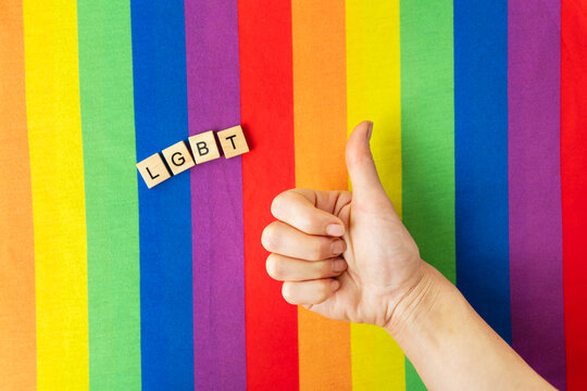 Close-up of an LGBT flag with a hand showing like. support and tolerance. Inscription with wooden letters LGBT.