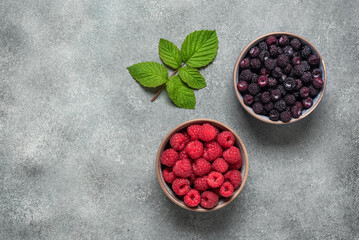 Raspberries black and red in a bowl on a gray concrete background. Top view, copy space.