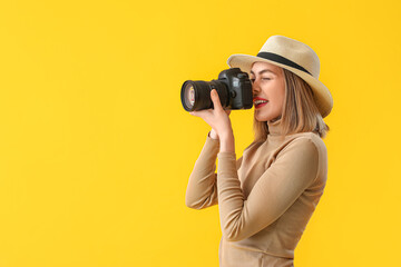 Female photographer with professional camera on yellow background