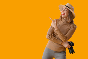 Female photographer with professional camera pointing at something on yellow background