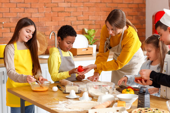 Female chef with group of little children preparing pizza during cooking class in kitchen