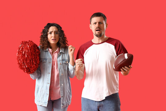 Upset young couple with rugby ball and pompom on red background