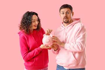 Young couple with piggy bank on pink background