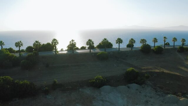 Aerial shot of a driveway with palms near the sea, drone footage. Rhodes, Greece. Beautiful mountain view next to The Mediterranean sea.