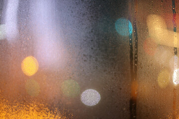 Soft focus blur water rain drops on wet window glass with city lights.