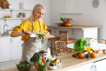 Mature woman with cut avocado making healthy smoothie in kitchen