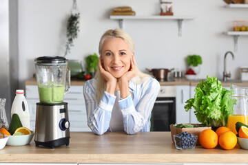 Mature woman making healthy smoothie with blender in kitchen
