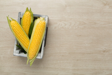 Fresh corn on cobs on wooden background, top view