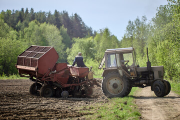 Potato planter is hitched to wheeled agricultural tractor in farmer field.