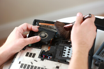 Repaiman with brush is cleaning disassembled laptop parts. Technical support and fixing gadgets problems. Servicing, repairing, cleaning, maintaining computers. Repair shop. Hardware maintenance