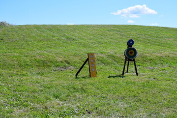 A close up on a shooting range located in the middle of a vast field or meadow next to some hay bales, with targets, bows, arrows, flags and other equipment  visible on a sunny summer day