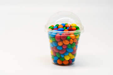 Multi-colored round candies in a transparent cup on a white background. Peanuts in chocolate.