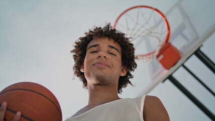 Smiling sportsman holding ball at stadium. Basketball player posing at street