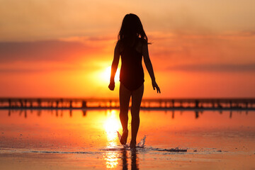 Silhouette of active little child girl in swimsuit is having fun runs and plays on a beach at sunset on summer travel holiday. Youth, lifestyle and happiness concept. Happy childhood. Copy space