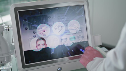 Beautician touching device screen choosing mode rejuvenation procedure close up.