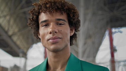 Elegant guy smiling camera at street closeup. Curly hair model posing portrait