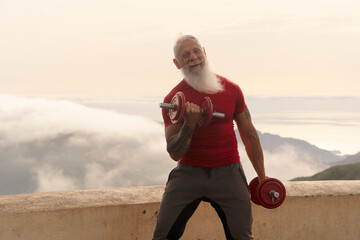 Senior man with white beard doing sport exercises with two dumbells outdoor, close up view, healthy...