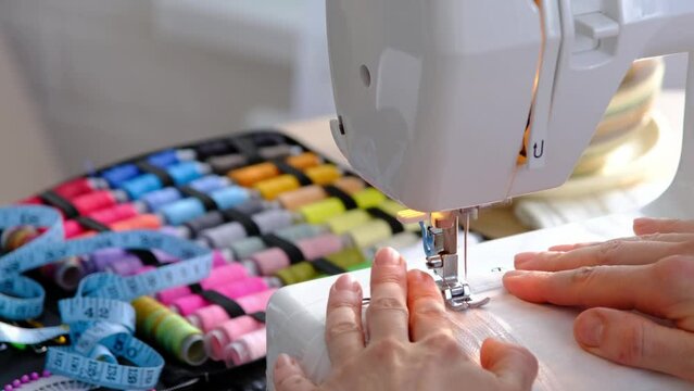 Woman hand close up sews tulle on electric sewing machine. Filling the thread into the sewing needle, adjusting the tension. Comfort in the house, a housewife's hobby, layout of sewing tools