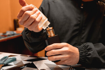 The technician's hands holding a vape while loading the liquid into the tank.