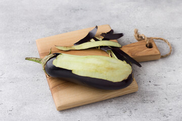 A whole eggplant with the skin removed on a wooden board on a gray textured table. Cooking delicious vegan food
