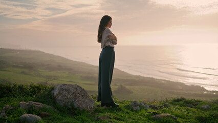 Young woman standing hill looking on seascape with sunset. Model posing seacoast