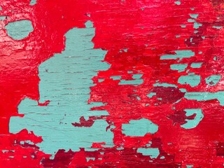 Grunge background, texture of old wooden surface with peeling paint, closeup. Aged pale blue cracking paint with bright red flaking layer over it. Worn out, damaged paint on a wall or vintage object.