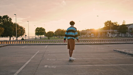Young man balancing skateboard at evening back view. Active guy riding longboard