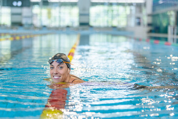 Portrait of a woman, a professional swimmer in black one-piece swimwear and a black cap with goggles