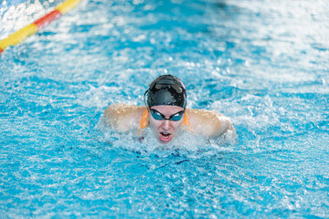 Female competitive swimmer moving through the water performing the butterfly stroke during swimming training, front view.