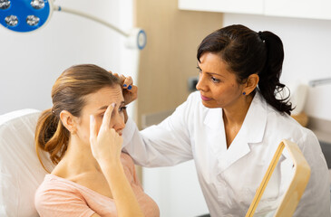 Woman cosmetologist and female client examining face skin after cosmetology beauty treatment at...