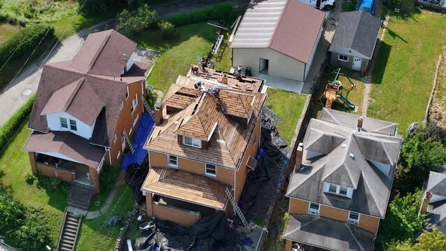 An aerial view of roofers putting on a new shingle roof on a typical middle class rust belt brick home.  	
