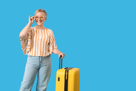Mature woman with suitcase on blue background