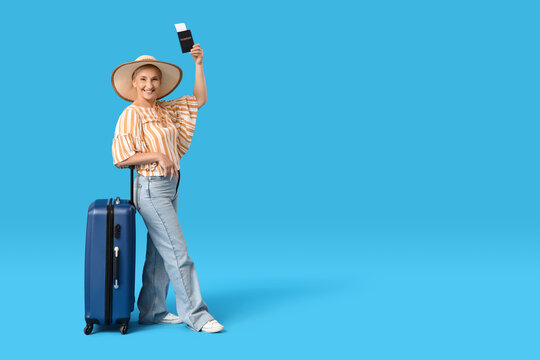 Mature woman with passport and suitcase on blue background