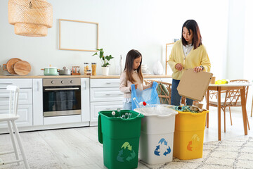 Asian mother with her little daughter sorting garbage with recycle bins in kitchen