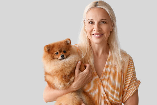 Mature woman with Pomeranian dog on light background