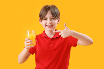 Little boy pointing at glass of orange juice on color background