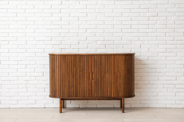 Wooden chest of drawers near light brick wall in room