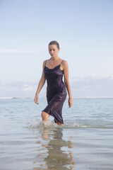Fototapeta na wymiar Creative portrait of female model in wet purple satin dress on the beach, stylish and elegant summer fashion
