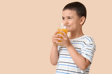 Cute little boy drinking orange juice on beige background