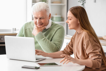 Senior man with his granddaughter using laptop in kitchen
