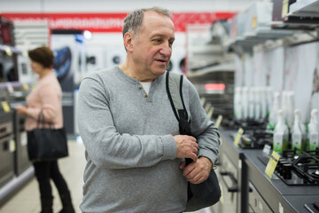 Naklejka na ściany i meble Portrait of a confident European man of mature age, who came to the electronics and household appliances store for a ..purchase, in the gas stoves department
