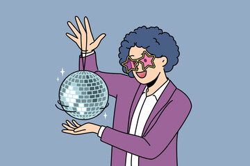Funny man with disco ball with curly wig on head came to nightclub or dance floor to have fun and relax. Young guy enjoys atmosphere of music festival or disco party for party people