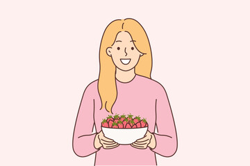 Woman holds plate of strawberries and smiles, offers to try fresh berries and farm fruits