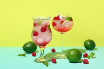 Glass of fresh raspberry mojito and limes on colorful background
