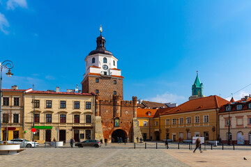Picturesque Lublin cityscape with historic symbol of city - medieval brick gate Brama Krakowska in sunny spring day, Poland - obrazy, fototapety, plakaty