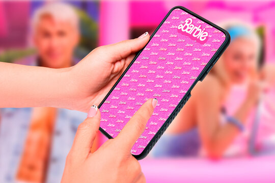 Buenos Aires, Argentina; 08-03-2023: Barbie the movie. Thematic horizontal background of woman's hands holding a cell phone that represents the success and fury for the Barbie movie.