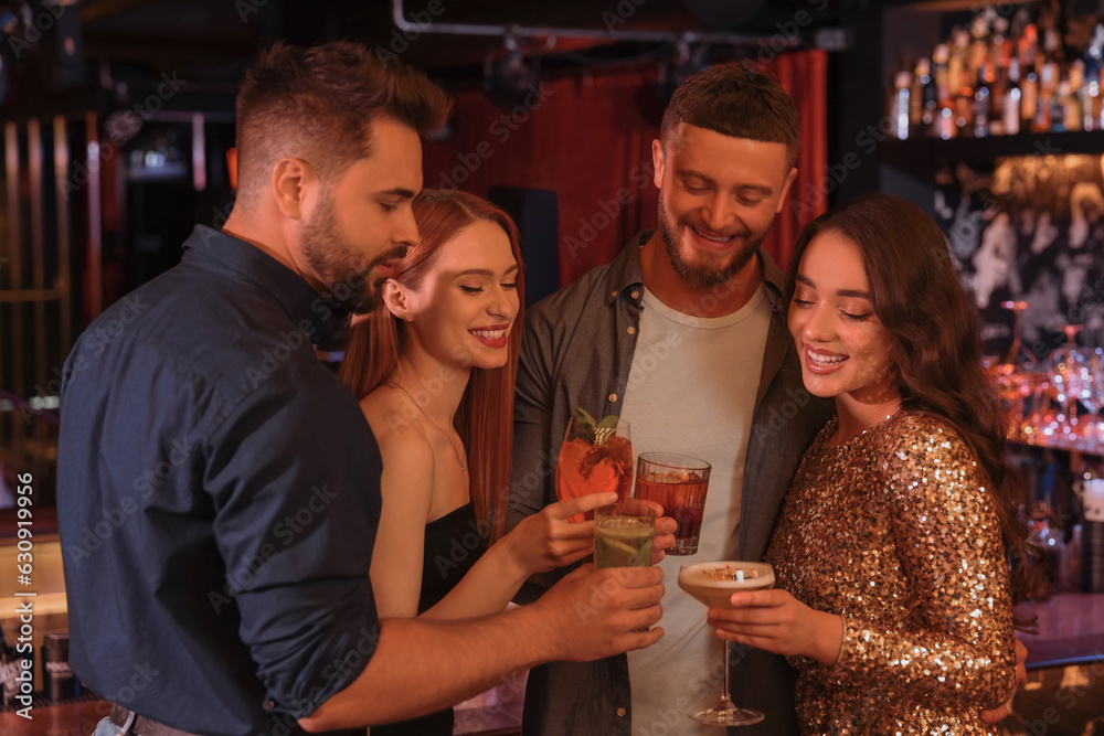 Poster Happy friends clinking glasses with fresh cocktails in bar