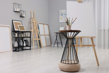 Wooden easel with canvas near paints and brushes in artist's studio, space for text