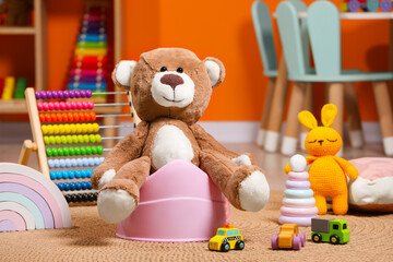 Teddy bear on pink baby potty and many other toys in room. Toilet training