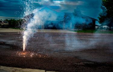 A fountain of sparks, flames, and smoke emitting from a fountain fireworks being set off in a residential neighborhood. 